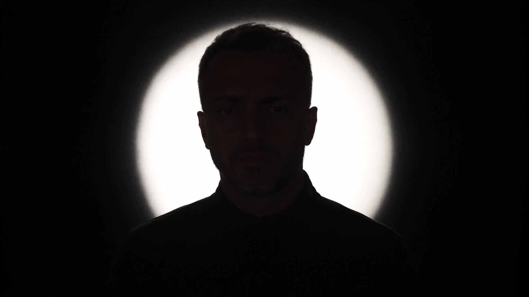 Alex Konstantinidis, backlit against a circle of light